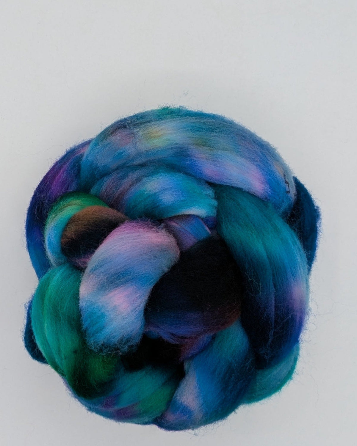 A knotted bundle of vibrant, marbled yarn in shades of teal, blue, purple, and green, displayed on a white square card against a textured gray background.