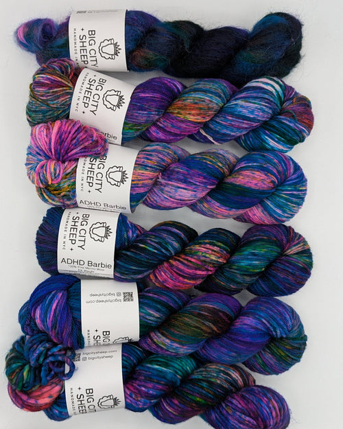 Six skeins of variegated yarn laid out on a white surface. The yarns feature multicolor variegation with shades of purple, blue, pink, and teal.