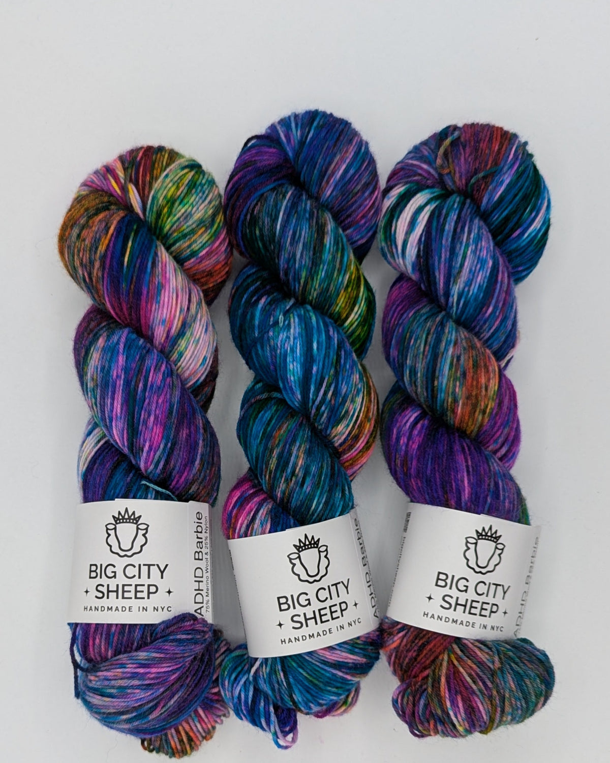 Three skeins of variegated yarn in vibrant shades of blue, purple, pink, green, and orange, arranged vertically on a white background.