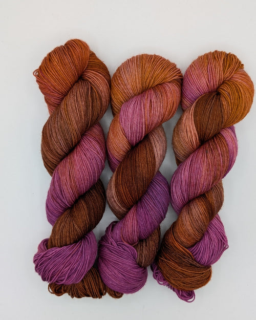 Three skeins of variegated yarn with a color-shifting gradient from deep purple to warm rust brown, displayed on a clean white background.