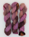 Three twisted skeins of variegated alpaca silk yarn in shades of purple, pink, brown, and orange on a plain white background.