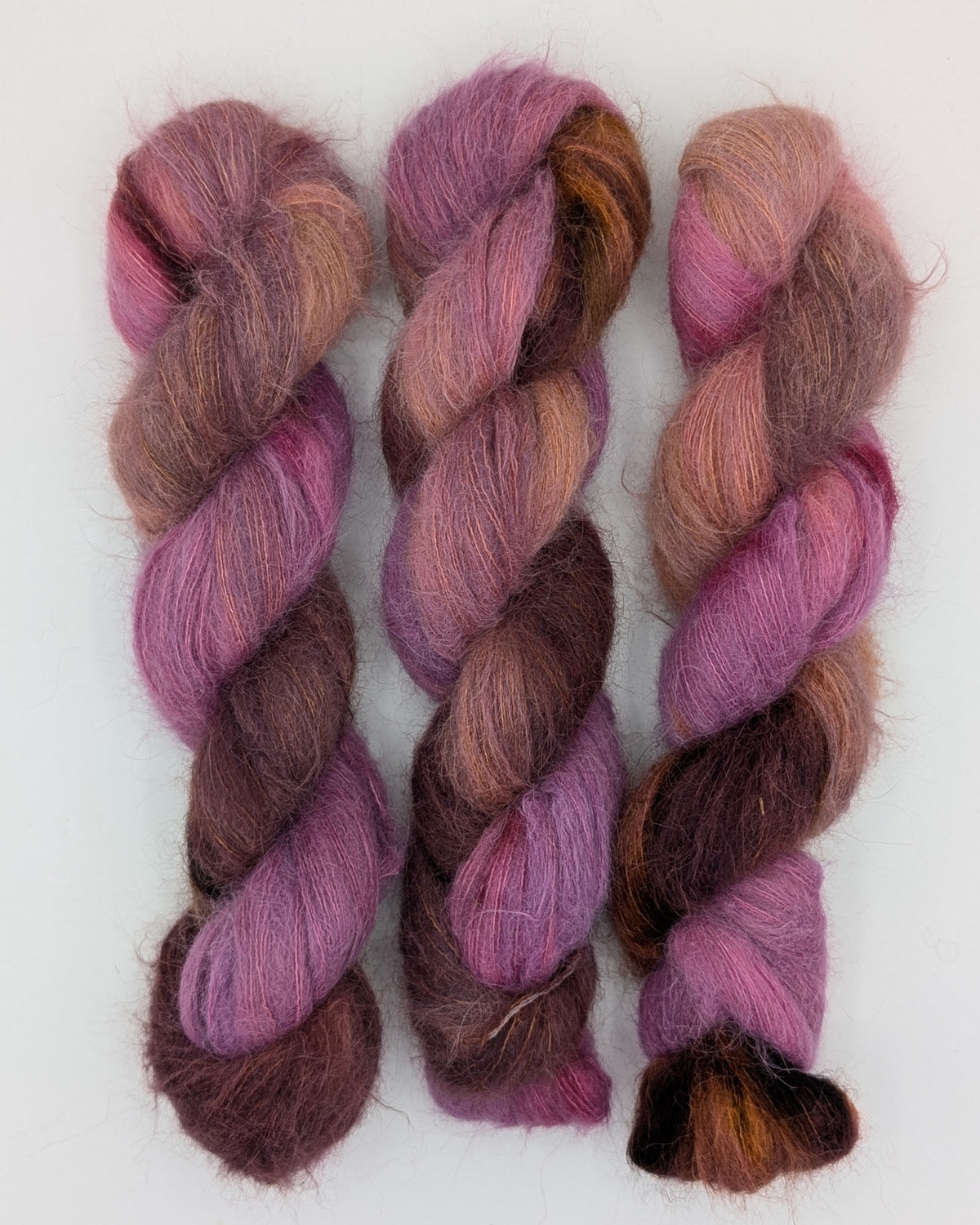 Three twisted skeins of variegated alpaca silk yarn in shades of purple, pink, brown, and orange on a plain white background.