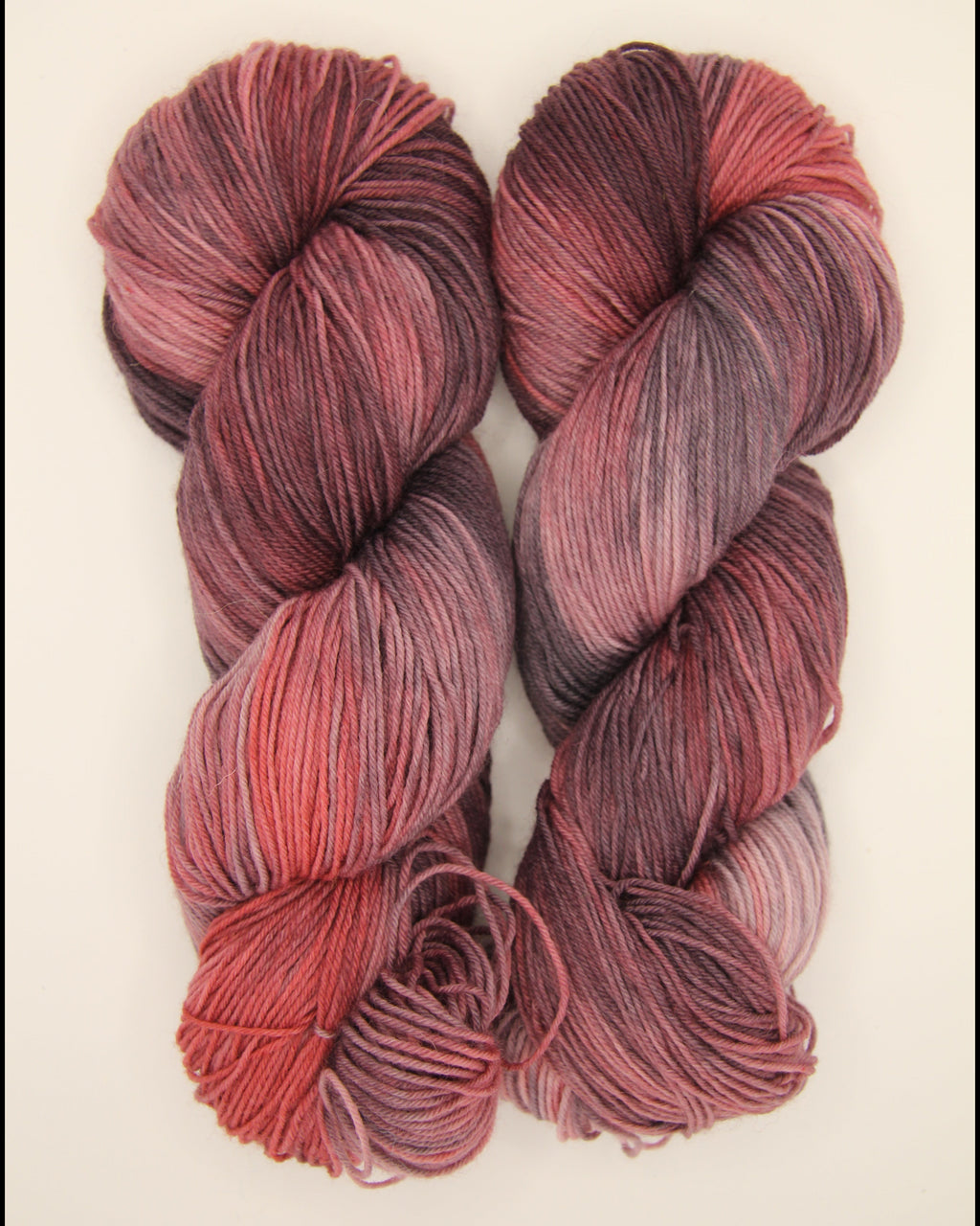 Two skeins of variegated yarn on a plain off-white background. The yarn features a color-shifting gradient transitioning from bright red to deep burgundy to a charcoal black.