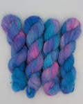 Four twisted hanks of alpaca silk variegated yarn in shades of blue, purple, and pink, arranged side-by-side on a plain white surface.
