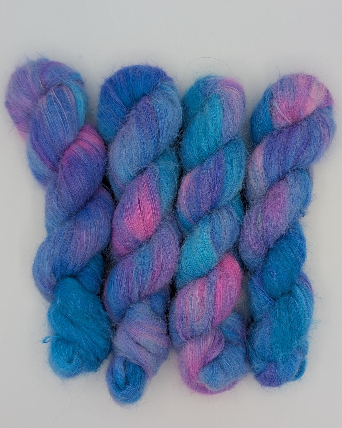 Four twisted hanks of alpaca silk variegated yarn in shades of blue, purple, and pink, arranged side-by-side on a plain white surface.