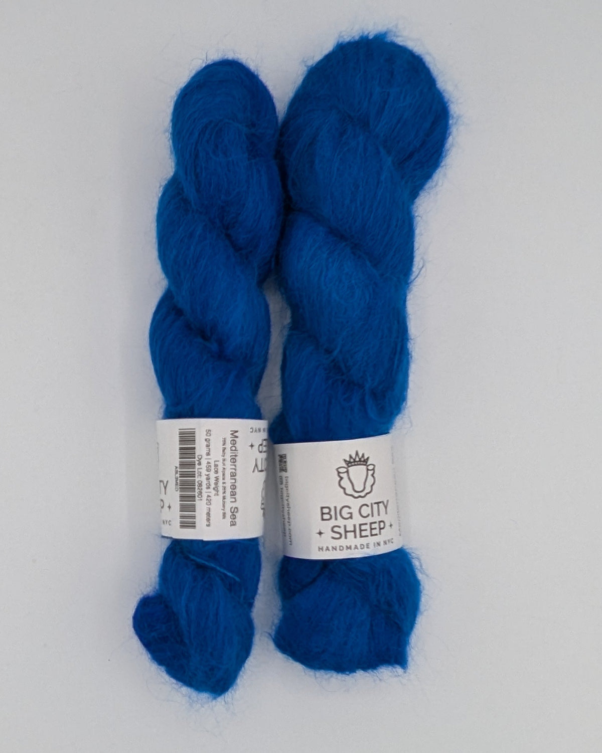 Two skeins of vibrant royal blue wool from Big City Sheep, displayed side-by-side inside a white box.