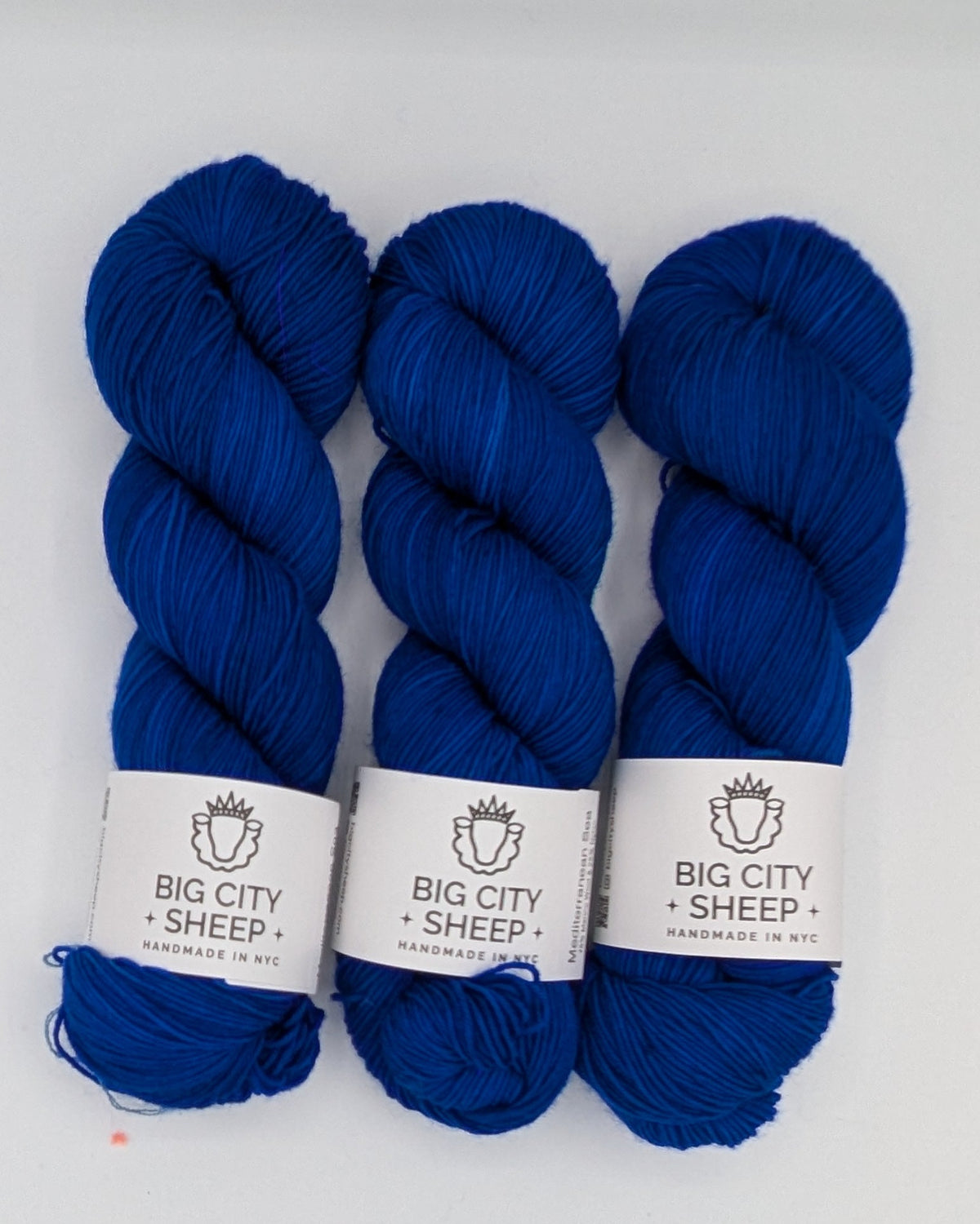 Three skeins of deep blue yarn with white paper labels reading 'BIG CITY SHEEP' arranged on a white surface.