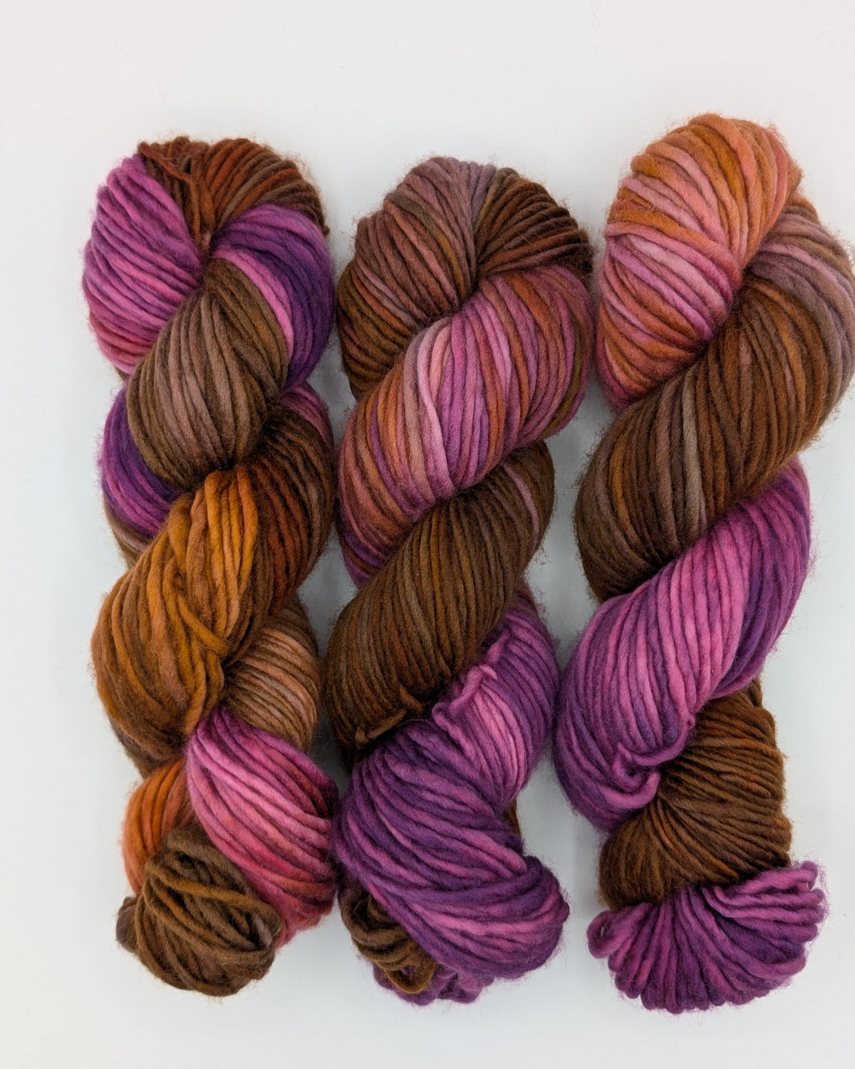 Three twisted skeins of chunky yarn in a fade from purple to orange to brown.