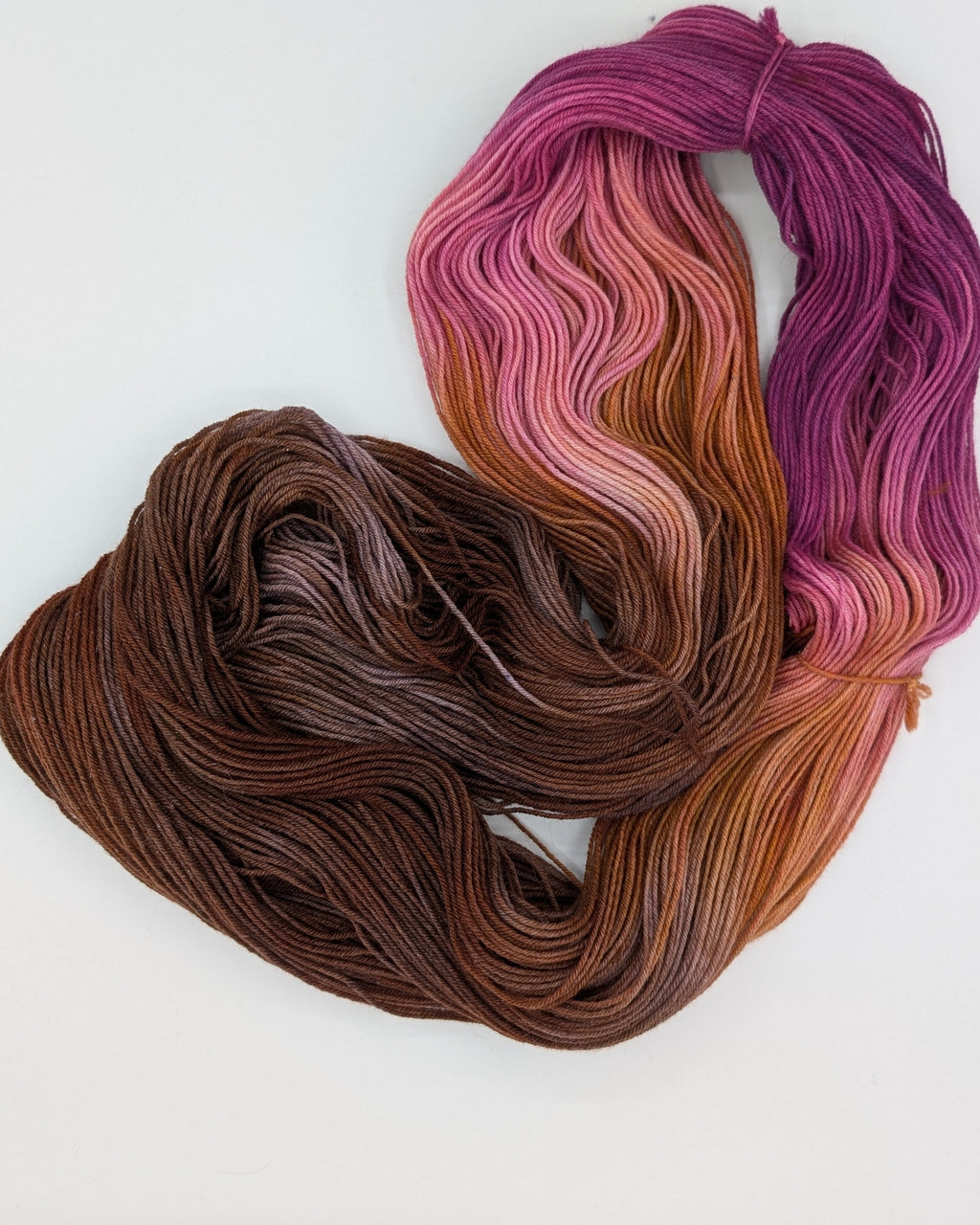 Three skeins of variegated yarn arranged on a plain white background, showing a color gradient from purple and pink through peach and orange to dark brown.