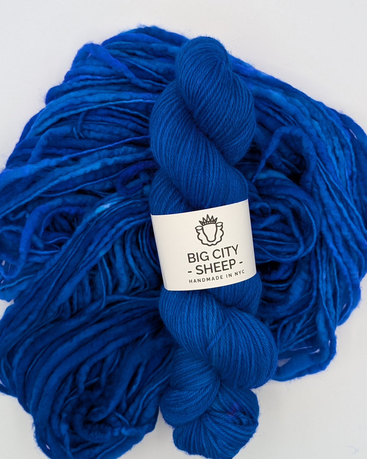A skein of vibrant royal blue yarn with a white paper label reading 'BIG CITY SHEEP', photographed on a clean white background.