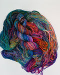 A skein of variegated yarn with multiple colors including teal, purple, pink, orange, and blue, arranged on a plain white background.