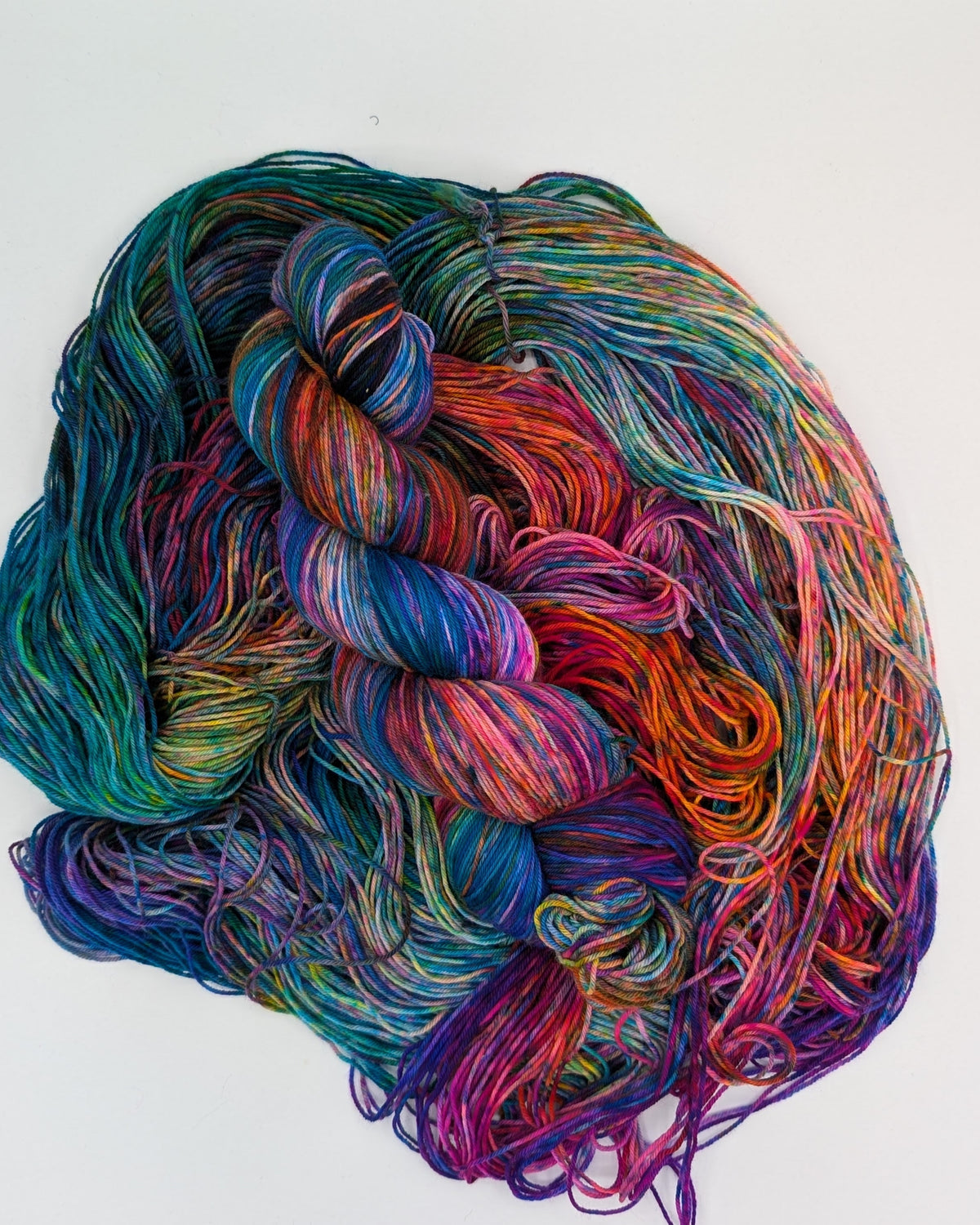 A skein of variegated yarn with multiple colors including teal, purple, pink, orange, and blue, arranged on a plain white background.