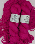 Two skeins of bright magenta pink yarn with white paper labels reading 'BIG CITY SHEEP' placed on a white surface.