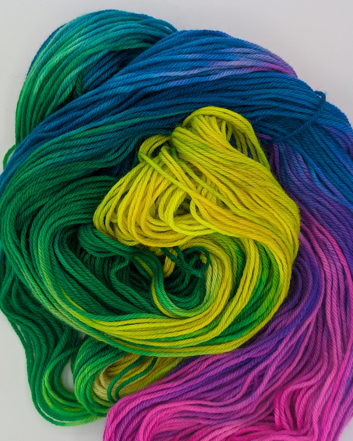 A skein of variegated yarn open in s spiral with a smooth color gradient transitioning through green, yellow, blue, and pink, photographed on a clean white background.