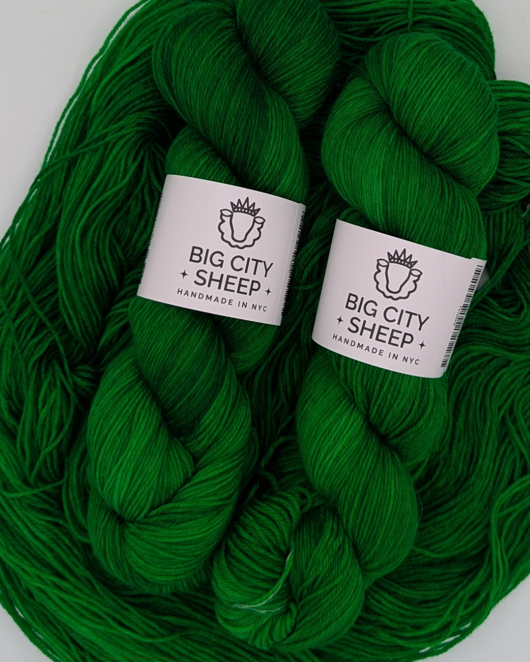 Two bright green skeins of yarn with white paper labels reading 'BIG CITY SHEEP HANDMADE IN NYC' on a plain white background.