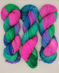 Three twisted hanks of variegated yarn in bright pink, teal, and blue, arranged side by side on a plain off-white background.