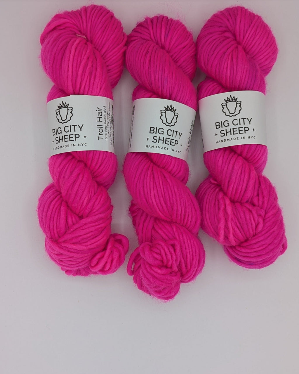Three skeins of chunky bright pink yarn with white paper labels reading 'BIG CITY SHEEP' arranged side by side on a white surface.
