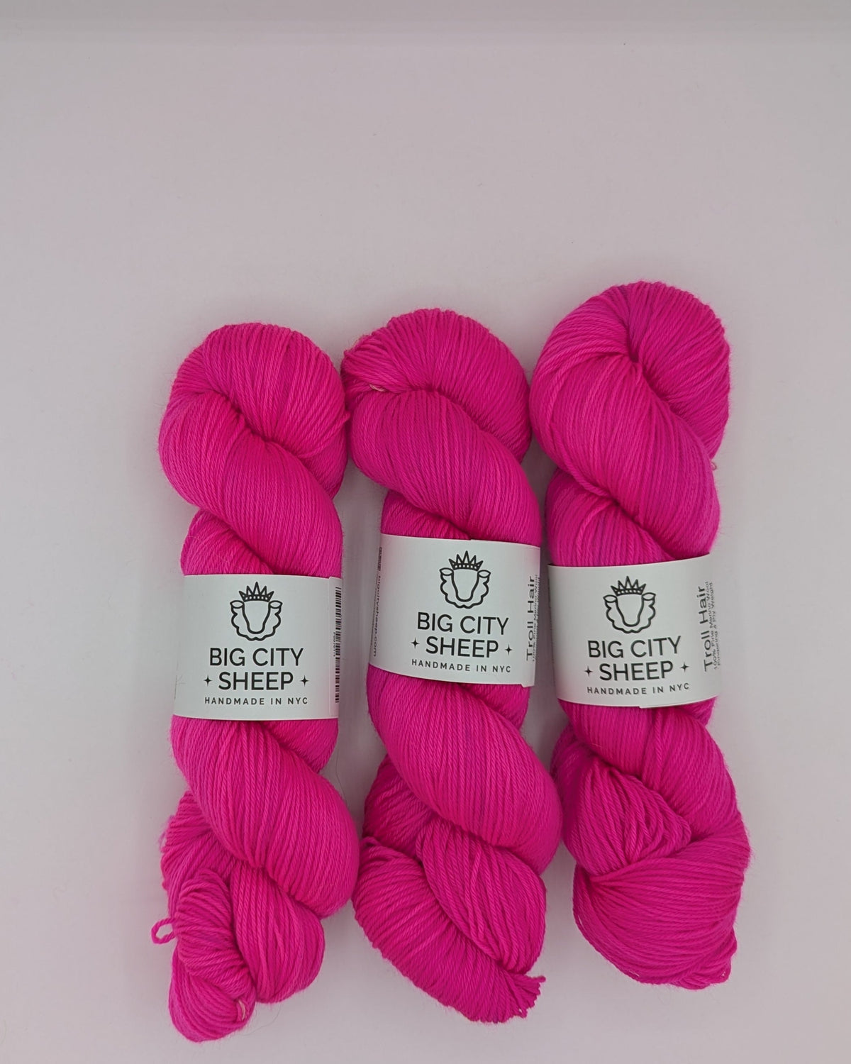 Three skeins of bright pink yarn with white paper bands reading 'BIG CITY SHEEP' arranged on a white surface inside a box.