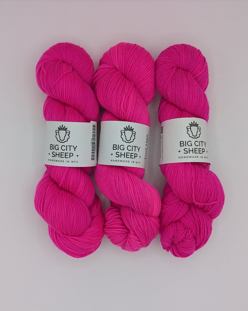 Three skeins of bright pink yarn with white paper labels reading 'BIG CITY SHEEP' arranged side by side inside a white box.