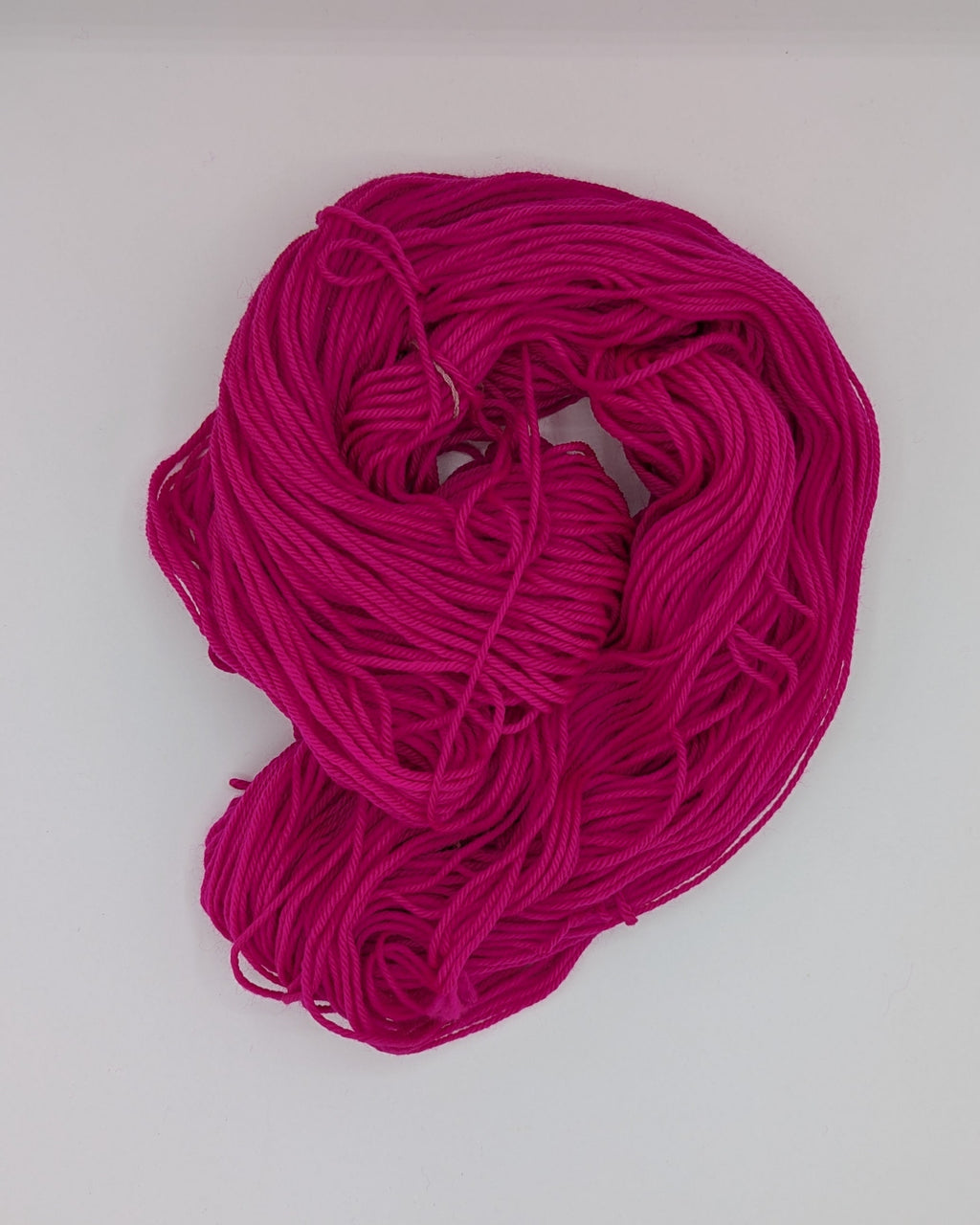 A bundle of bright magenta pink yarn or cord laid on a white surface.